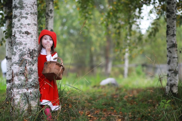 Une petite fille avec un chapeau rouge et des robes se promène dans le parc Cosplay pour le héros de conte de fées Le Petit Chaperon Rouge