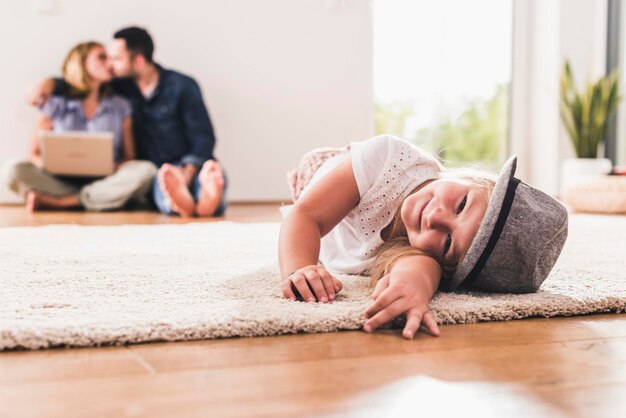 Petite fille avec chapeau s'amusant à la maison, parents utilisant un ordinateur portable en arrière-plan