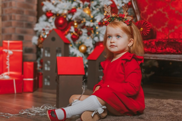 petite fille charismatique dans une robe rouge sur le fond des décorations de Noël