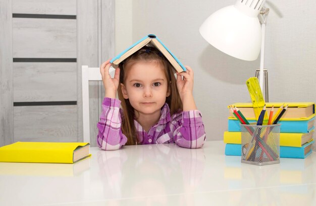 Une petite fille charmante tient un livre dans ses mains. fait ses devoirs à la maison. Mise au point sélective.