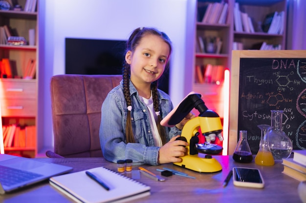 Une petite fille en chemise denim qui apprend la science le soir à la maison.