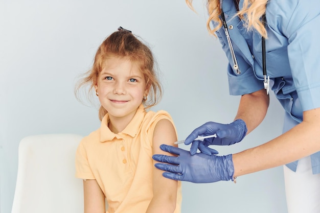 Photo petite fille en chemise jaune médecin en uniforme faisant la vaccination au patient
