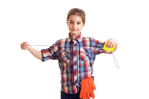 Petite fille en chemise rouge à carreaux avec des gants orange et des lunettes tenant un tournevis et une roulette