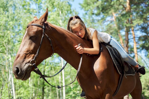 Petite fille à cheval, balade à cheval d'été dans la forêt, fille amoureusement étreinte de cheval.