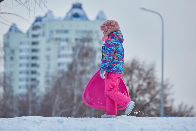 Petite fille à cheval sur la neige glisse en hiver