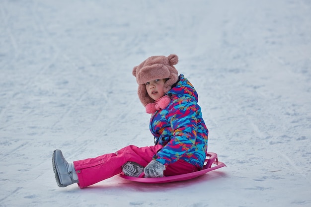 Petite fille à cheval sur la neige glisse en hiver