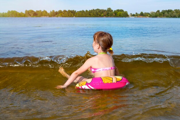 Une petite fille chevauchant un cercle gonflable sur les vagues d'une rivière par une journée ensoleillée