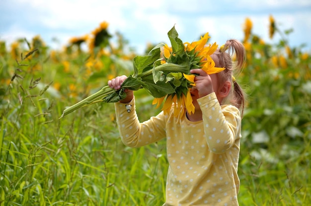 Petite fille Cheveux blonds Jour d'été Tournesols en fleurs renifle l'enfant Sans visage