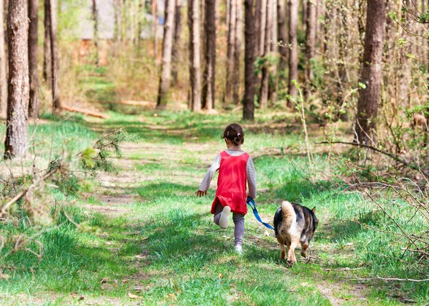 Petite fille avec un chien qui court dans les bois