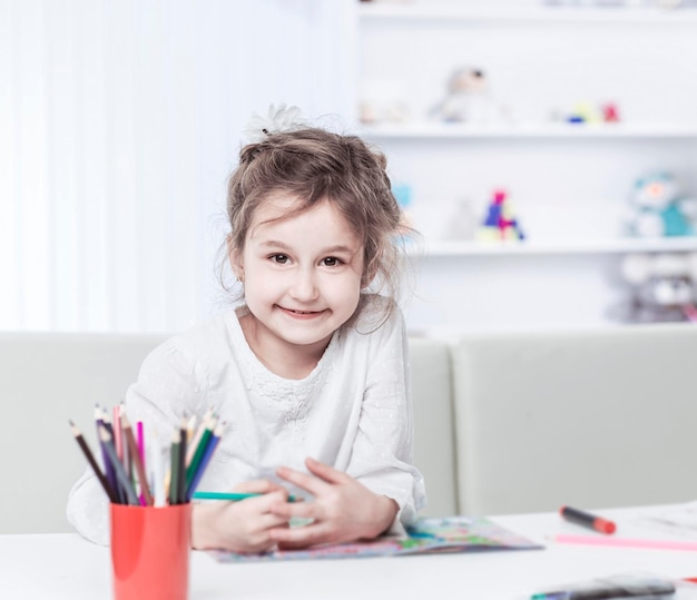 Petite fille de cinq ans dessine avec des crayons assis à table dans la pépinière