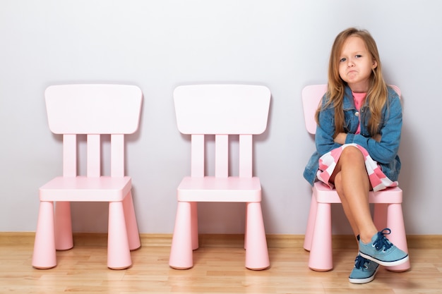 Petite fille en colère assise sur une chaise.