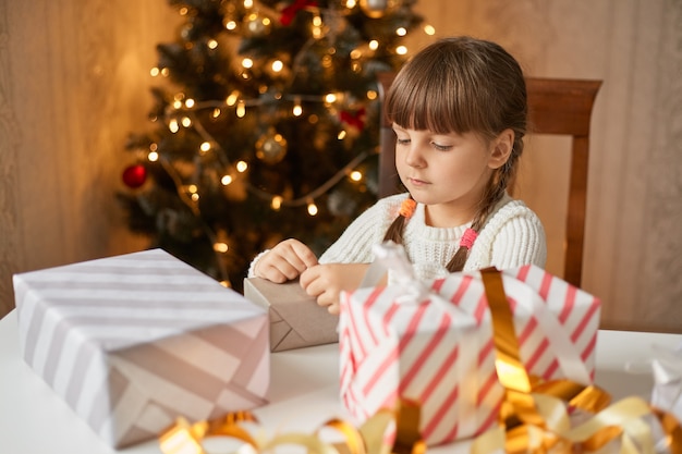 Petite fille concentrée avec deux nattes assis à table et emballage boîte de Noël