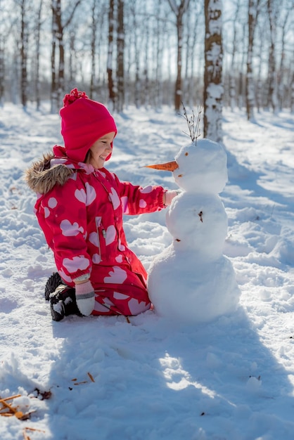 Petite fille construisant un bonhomme de neige dans un parc enneigé Loisirs actifs en plein air en famille avec enfants en hiver Enfant pendant une promenade dans un parc d'hiver enneigé