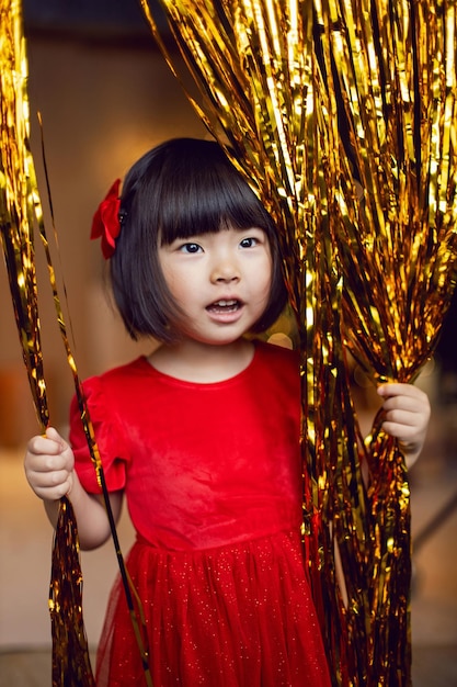 Une petite fille coréenne en robe rouge joue la nuit de Noël avec des guirlandes dorées