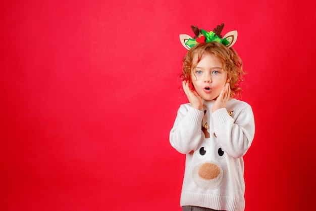 Petite fille en cornes de cerf sur fond rouge, Noël, nouvel an