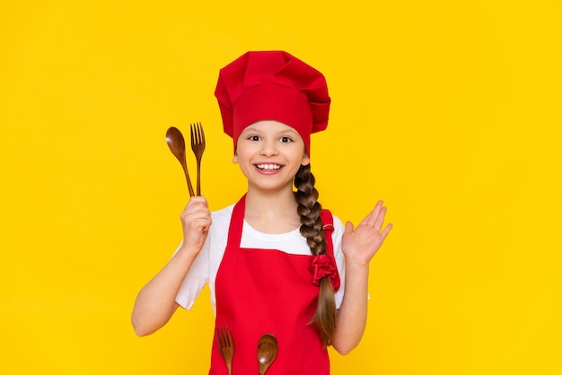 Une petite fille en costume de cuisinier un bébé cuisinier petit-déjeuner en costume de chef Concept de cuisine une fille cuisiner sur un fond jaune isolé