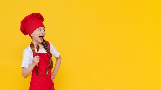 Une petite fille en costume de cuisinier un bébé cuisinier petit-déjeuner en costume de chef Le concept de déjeuner de cuisine une fille cuisine sur un fond jaune isolé avec espace de copie