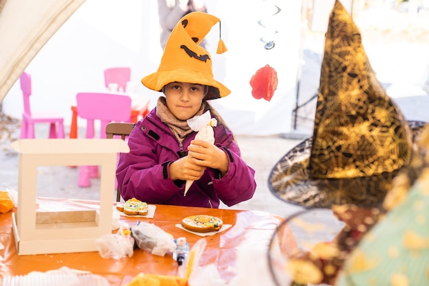 Une petite fille en costume d'Halloween joue avec des biscuits au pain d'épice comme une citrouille.