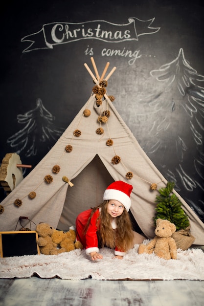 Petite fille en costume de père Noël pose dans les décorations de Noël