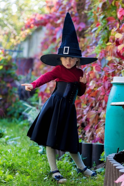 Petite fille en costume de sorcière posant sur la fête d'halloween dans le jardin.