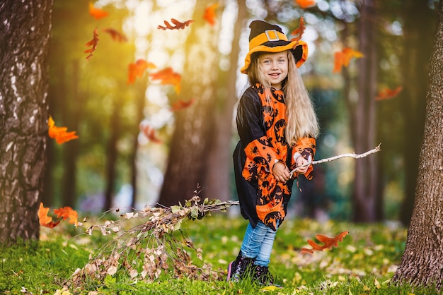 Petite fille en costume de sorcière vole sur un manche à balai dans le parc pour les vacances d'Halloween.