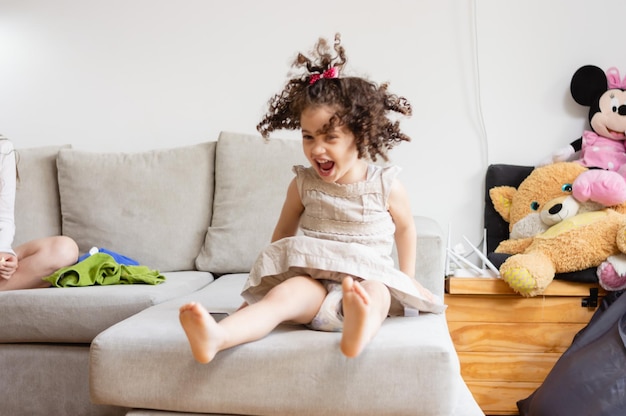 petite fille en couches criant heureux de sauter sur le canapé du salon