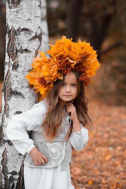 Une petite fille avec une couronne de feuilles et de baies sur la tête dans les bois