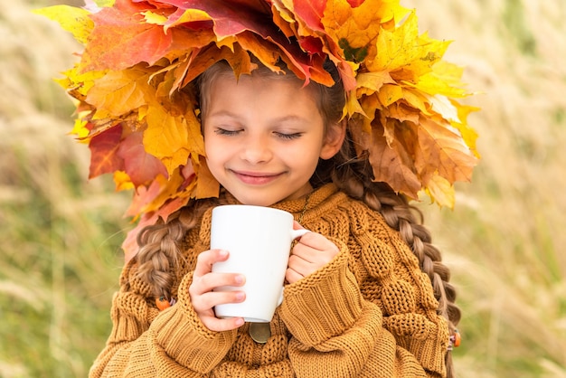 Une petite fille avec une couronne sur la tête boit un délicieux thé en automne.