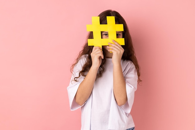 Petite fille couvrant le visage avec le symbole de hashtag des médias sociaux recommandant de suivre le contenu à la mode