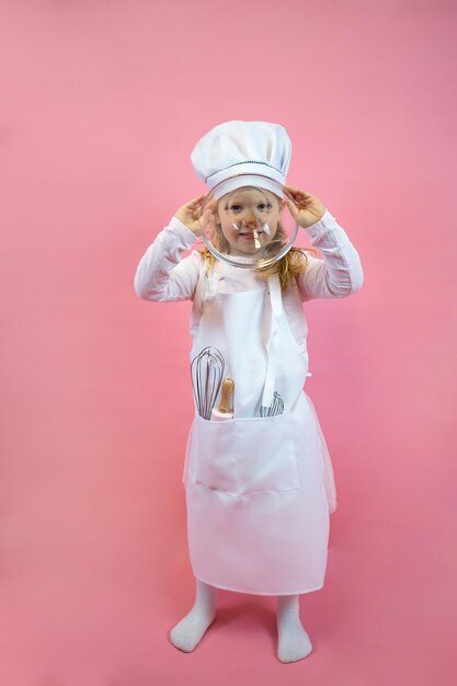 Petite fille cuisinière dans un tablier et une casquette, tient une tasse en verre et couvre son visage, affiche, carte postale, nourriture.