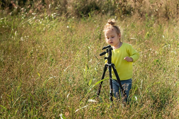 petite fille curieuse aux cheveux blonds ondulés joue avec un trépied pour des photos dans le parc