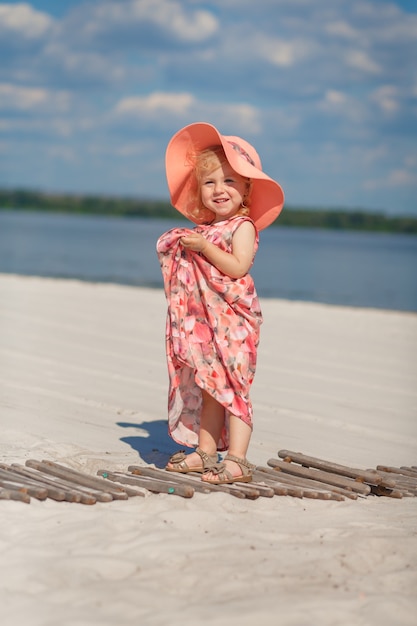 Une petite fille dans une belle sarafna joue dans le sable sur la plage.