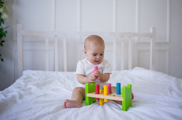 Petite fille dans un body blanc joue avec un jouet éducatif sur le lit