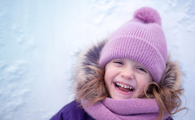 Une petite fille dans un bonnet tricoté et un snood rit allongé sur la neige
