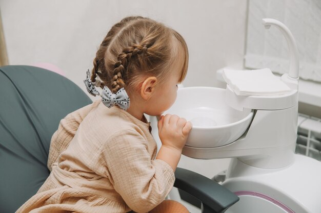 Une petite fille dans le cabinet du dentiste crache de la salive dans l'évier.