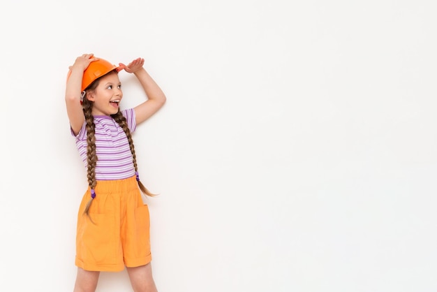 Une petite fille dans un casque de construction regarde votre annonce sur un fond blanc isolé Espace de copie Le concept de rénovation dans la chambre des enfants