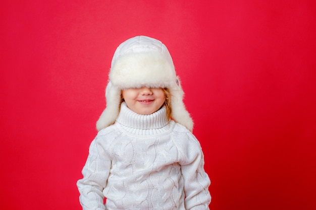 Une petite fille dans un chapeau d'hiver sur un fond rouge sourit