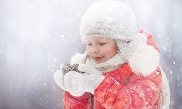 une petite fille dans un chapeau moelleux marche un jour d'hiver enneigé