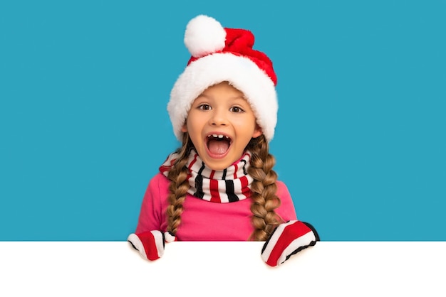 Une petite fille dans un chapeau de Noël regarde derrière votre publicité.