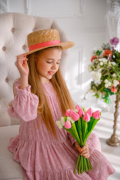 Une petite fille dans un chapeau de paille tient un bouquet de fleurs printanières à la maison