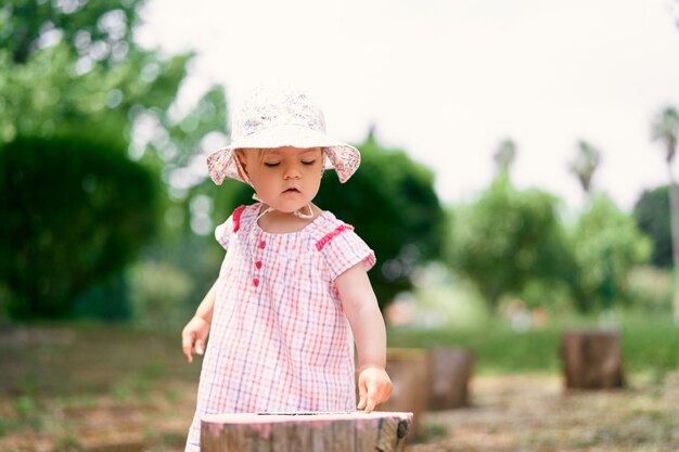 La petite fille dans un chapeau de panama se tient sur la pelouse près de la souche