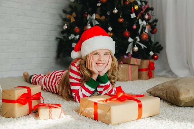 Petite fille dans un chapeau de père Noël se trouve près de l'arbre de Noël à la maison. vue d'en-haut. Noël.