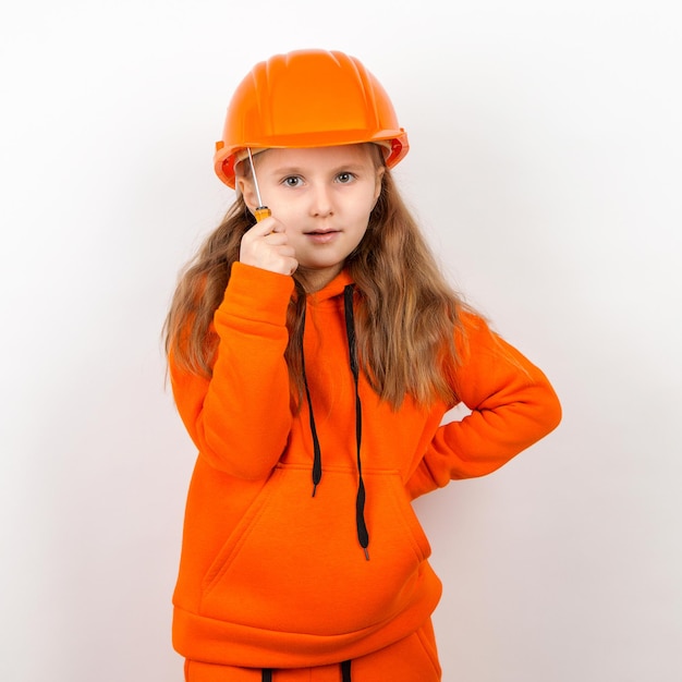 Une petite fille dans un costume orange et un casque de construction tenant un tournevis un concept d'un jeune travailleur Portrait fond blanc Fête du travail
