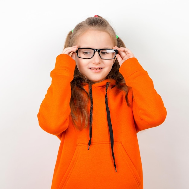 Une petite fille dans un costume orange et des lunettes Emotions un portrait sur fond blanc