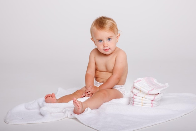 Petite fille dans une couche avec une pile de couches sur un fond blanc