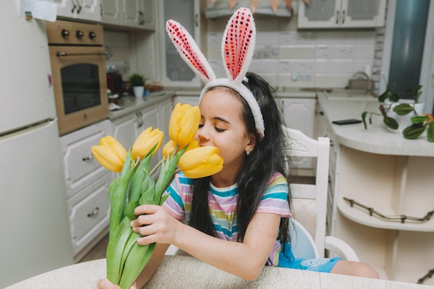 Petite fille dans la cuisine en oreilles de lapin avec un bouquet de tulipes tradition de pâques