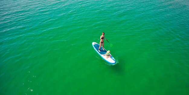 Petite fille dans un gilet de sauvetage assis sur le paddle board avec sa mère