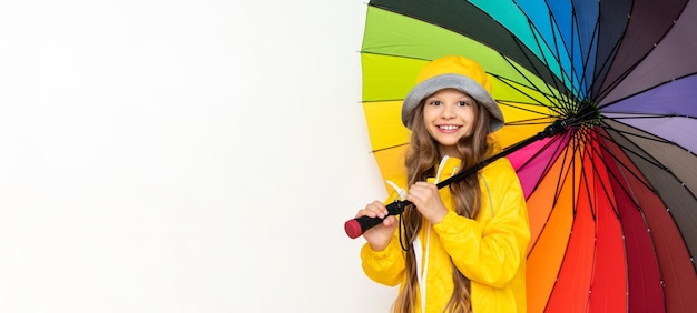 Une petite fille dans un imperméable tient un parapluie multicolore sur un fond blanc isolé