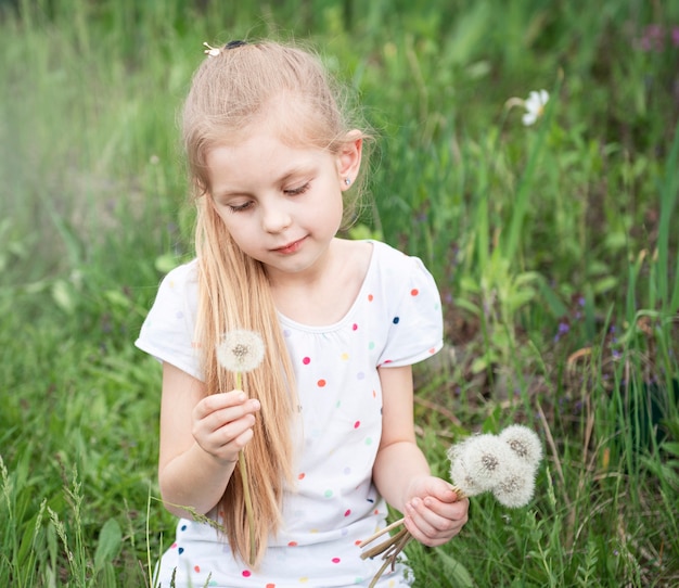Petite fille dans un jardin de printemps avec des pissenlits blancs dans ses mains