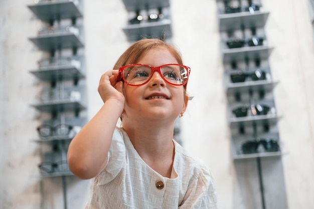 Petite fille dans le magasin de lunettes choisissant des lunettes